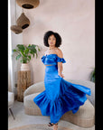Model wearing a royal blue satin off-shoulder crop top and matching flared skirt in a minimalist living room setting.