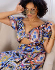 Model wearing multicolored open cut silk jumpsuit with puff sleeves and wide-leg design.