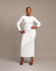 Woman wearing the Zola white maxi dress with bateau neckline, rhinestone embellishments, long sleeves, deep V-back plunge, and hemline slit.