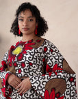 Woman wearing a bold Ankara two-piece set with flared sleeves and a fitted skirt in red, yellow, and black floral prints.

