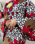 Woman wearing a bold Ankara two-piece set with flared sleeves and a fitted skirt in red, yellow, and black floral prints.
