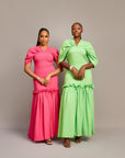 Two women wearing the Ine maxi dress in pink and green, featuring a draped V neckline, gathered waist detailing, and ruched hem accents.
