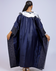 A woman wearing a metallic navy blue kaftan gown with an embroidered white floral neckline and wide sleeves, styled for special occasions.
