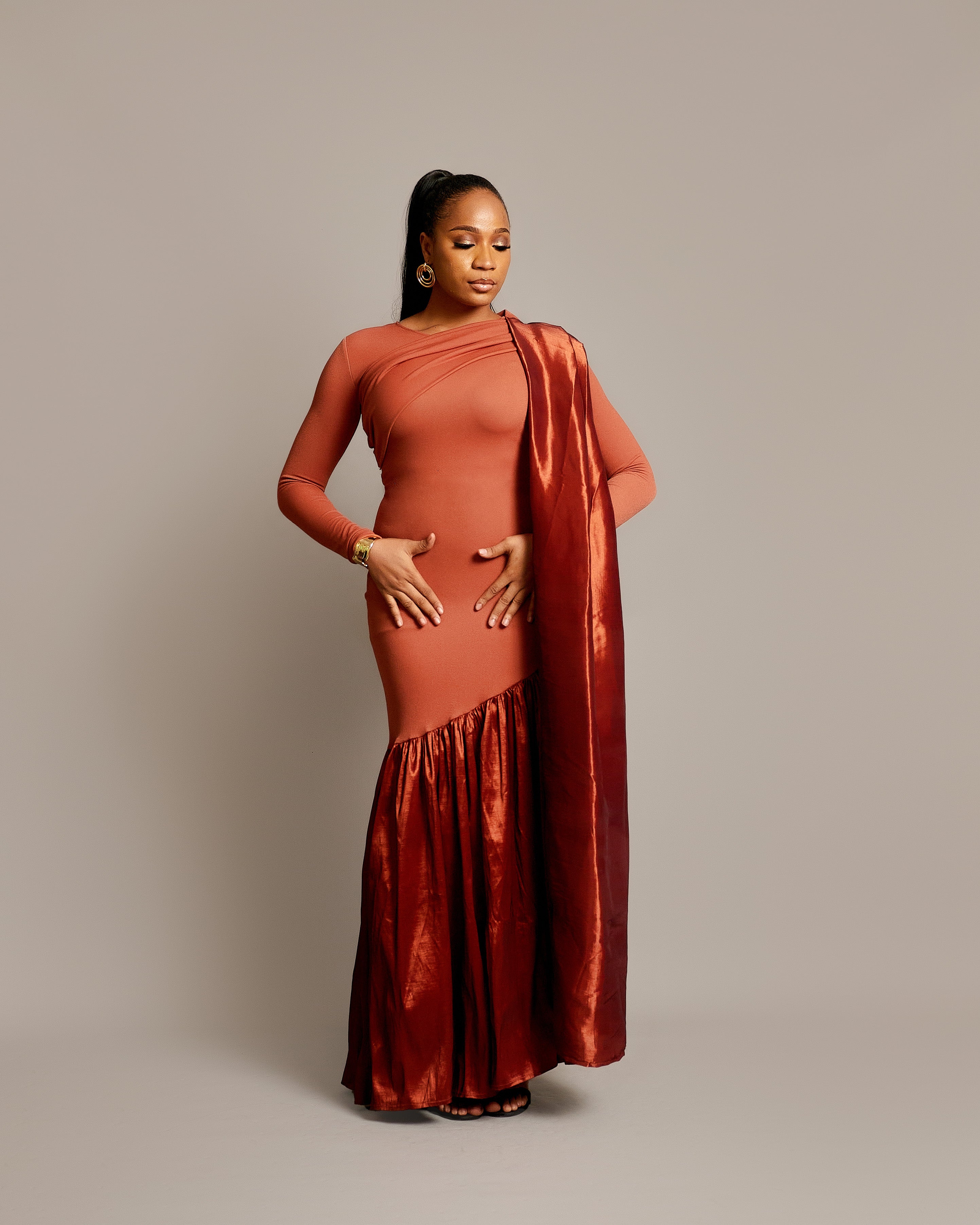 A woman wearing a rust sari dress with an asymmetrical neckline, gathered satin hem, and draped fabric over one shoulder.
