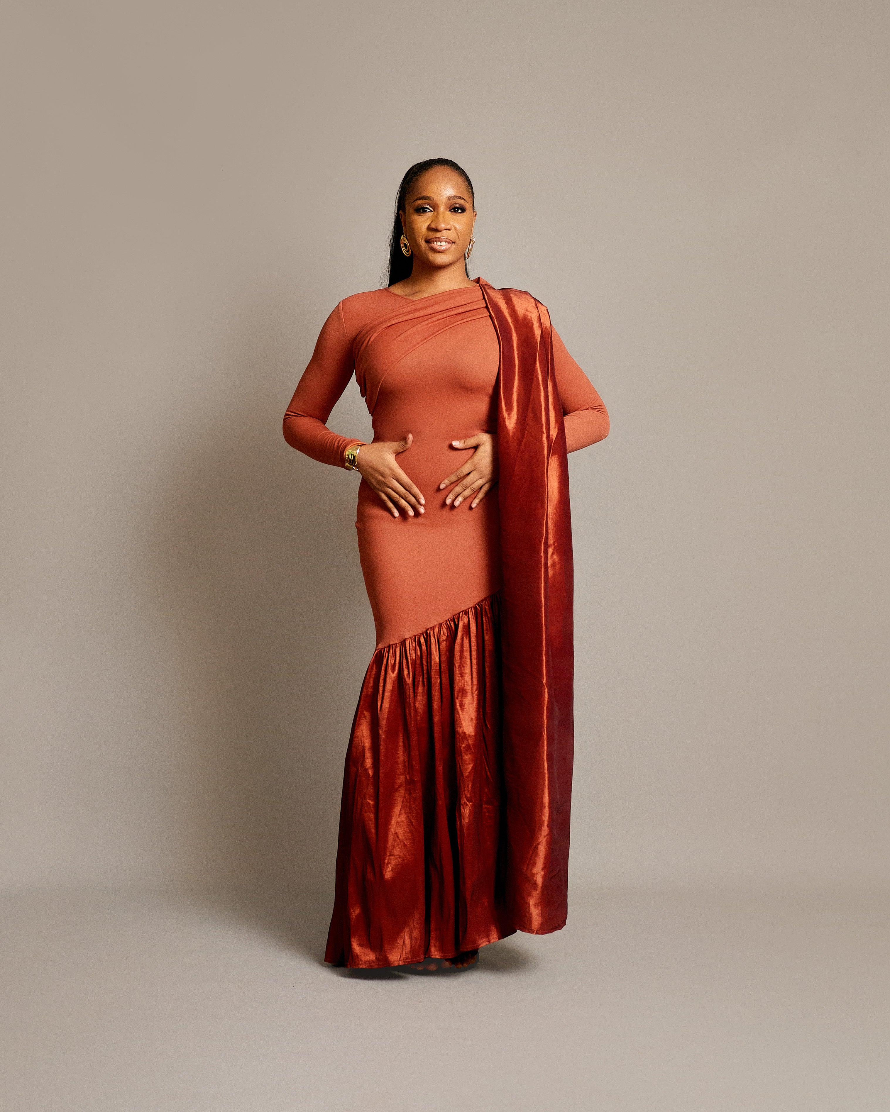 A woman wearing a sari dress with an asymmetrical neckline, gathered satin hem, and draped fabric over one shoulder.
