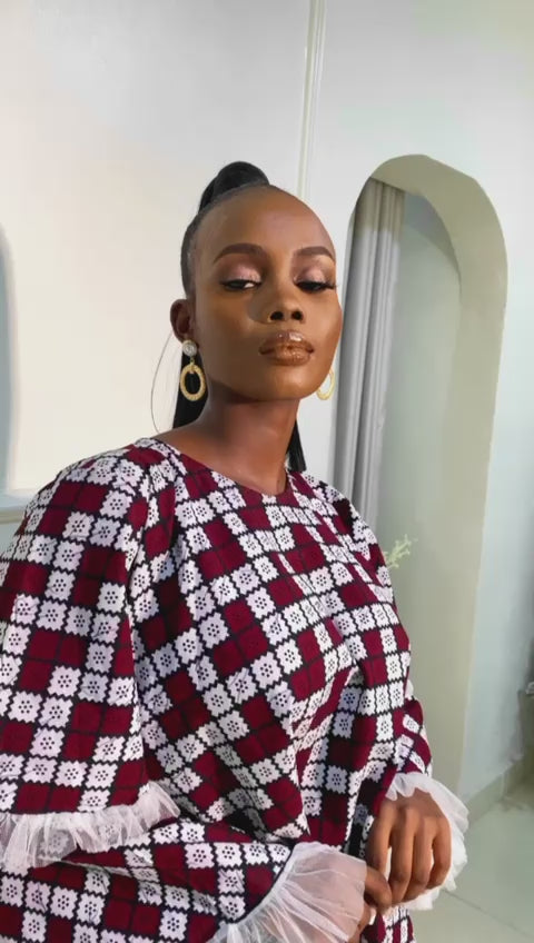 Model wearing a short flared Ankara dress with white lace sleeve detailing in a minimalist living room setting.
