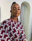 Model wearing a short flared Ankara dress with white lace sleeve detailing in a minimalist living room setting.
