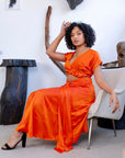  Woman wearing an orange satin crop top and matching ruched skirt, styled with statement glasses